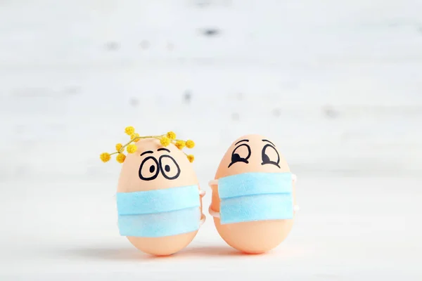?hicken eggs with funny faces in medicine masks and wreath of mimosa on white wooden background