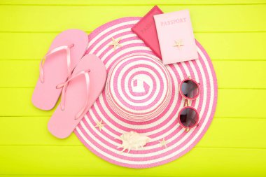 Yeşil ahşap masadaki terlikli, güneş gözlüklü, pasaportlu ve deniz kabuklu yaz hasır şapkası.