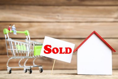 Ahşap ev modeli, alışveriş carf 'ı ve kahverengi arka planda satılan metin.