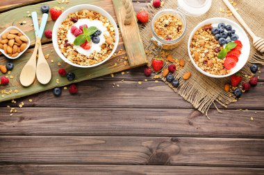 Kahverengi ahşap arka planda taze böğürtlen ve kaşıklarla lezzetli granola.