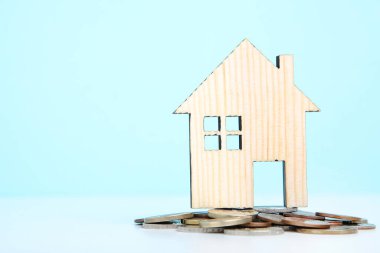 Mavi arka planda bozuk paraları olan ahşap ev modeli.