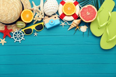 Hasır şapkalı bir çift parmak arası terlik, taze meyve, deniz kabuğu ve mavi ahşap arka planda güneş gözlüğü.
