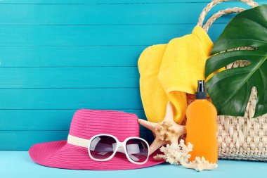 Güneş gözlüklü pembe şapka, sarı havlu, deniz yıldızları ve mavi ahşap arka planda canavar yaprağı.