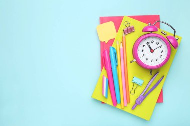 Mavi arka planda alarm saati olan okul malzemeleri.