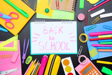 Farklı okul malzemeleri ve siyah arka planda okula dönüş metni.