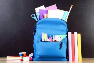 Siyah arka planda okul malzemeleriyle dolu sırt çantası.