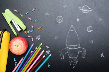 Tahta üzerine roket çizilmiş farklı okul malzemeleri.