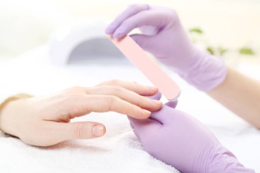 Eldivenli manikürcü. Tırnak törpüsüyle müşteriye manikür yapıyor.