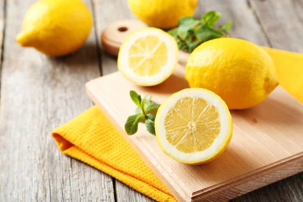 Lemons on cutting board on grey wooden background — Stock Photo, Image