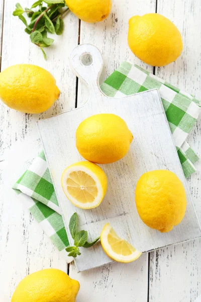 Lemons on cutting board on white wooden background — Stock Photo, Image