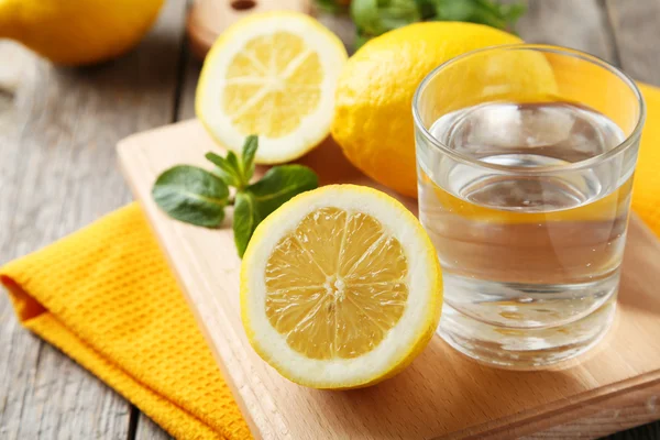 Limones en tabla de cortar con vaso de agua —  Fotos de Stock