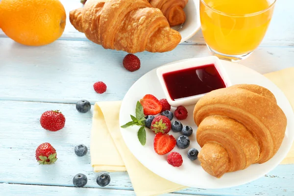 Verse smakelijke croissants met bessen op blauwe houten achtergrond — Stockfoto