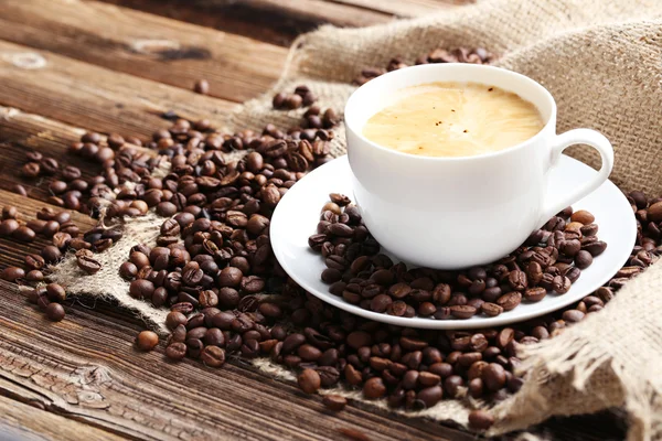 Tasse Kaffee mit Kaffeebohnen auf braunem Holzhintergrund — Stockfoto