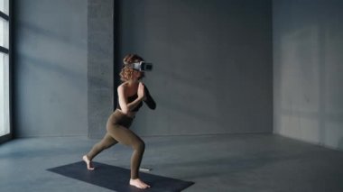 Sanal gerçeklik kulaklığı kullanarak stüdyoda yoga egzersizi yapan genç bir kadın.