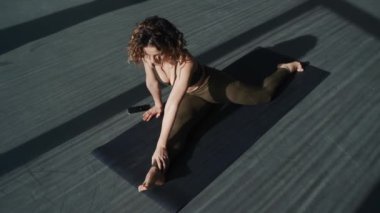 Güneşli bir günde, büyük panoramik pencerelerle stüdyoda yoga egzersizleri yapan genç bir kadının en iyi kamera görüntüsü.