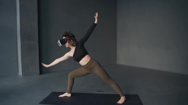 Ung kvinna som övar yoga i studio med hjälp av virtuella verklighetsglasögon — Stockvideo