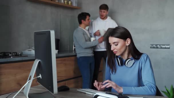 Jonge vrouw typt op de computer terwijl haar collega 's praten op de achtergrond. Teamwerkconcept — Stockvideo