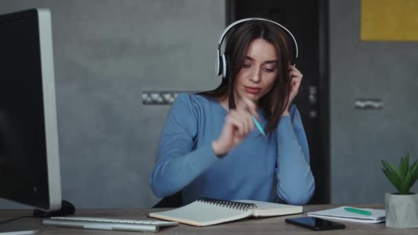 Mujer joven recibiendo videollamada, usando auriculares blancos y bloc de notas. Concepto de cuarentena de autoaislamiento — Vídeo de stock