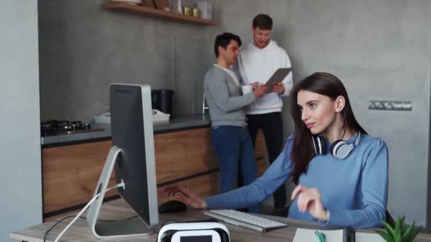 Jonge vrouw typt op de computer terwijl haar collega 's praten op de achtergrond. Teamwerkconcept — Stockvideo