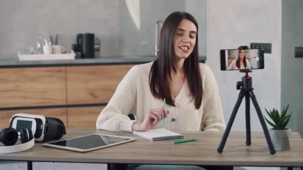 Jovem blogueira gravação de vídeo blog usando seu telefone celular no tripé na cozinha de sua casa. — Vídeo de Stock