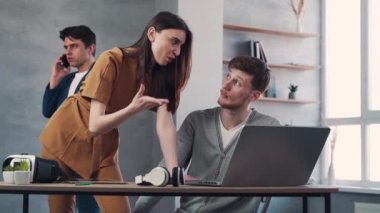 Man and woman discussing project while their colleague having a phone call behind. Teamwork concept