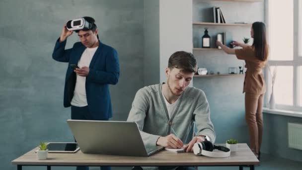 Teamwork in modern kantoor, man werkt met laptop terwijl zijn team een rem heeft — Stockvideo