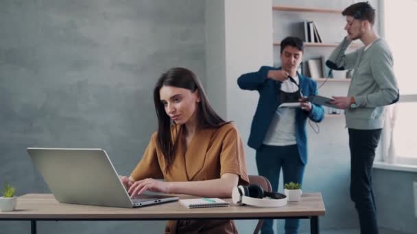 Giovane donna che lavora con il computer portatile mentre i suoi colleghi stanno parlando in background — Video Stock