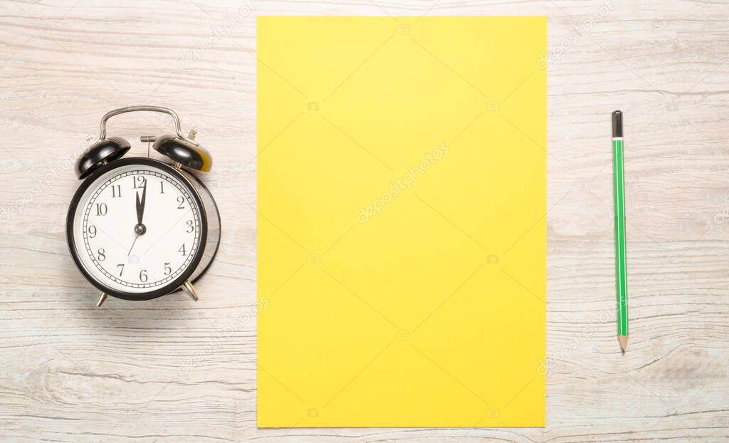 yellow blank card to write the text or resolutions for the new year with a clock and a pencil on a wooden background