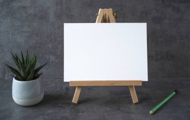 Beyaz yazı tahtası olan ahşap sehpa ve gri arka planda saksıdaki bitki.