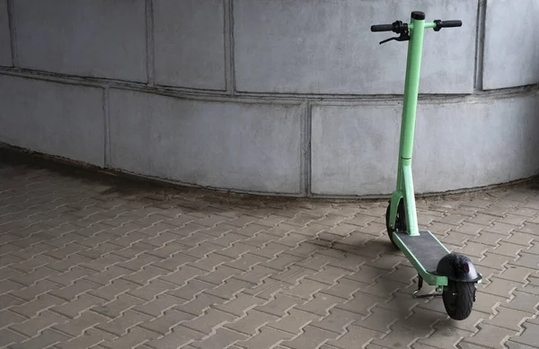 electric green scooter parked on the sidewalk next to the wall