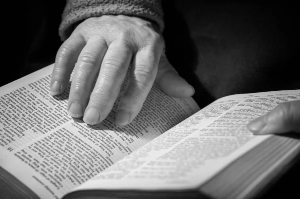 hands of elderly woman pray on bible