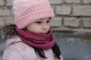 Şapkalı küçük güzel çocuk tuğla duvar arkasına bakıyor.