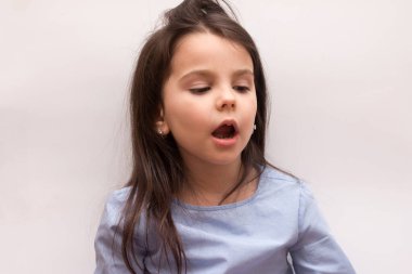 Saçları taranmış bir çocuk stüdyoda beyaz bir arka planda ağzı açık oturuyor.