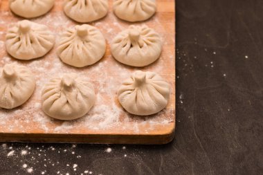 Mutfak tahtasının köşesinde un tarafından ezilmiş pürüzsüz Gürcü khinkali sıraları.