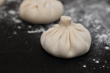 Siyah bir masaya un serpiştirilmiş üç çiğ Gürcü khinkali. Yan görünüm