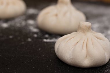 Siyah bir masaya un serpiştirilmiş üç çiğ Gürcü khinkali. Yan görünüm