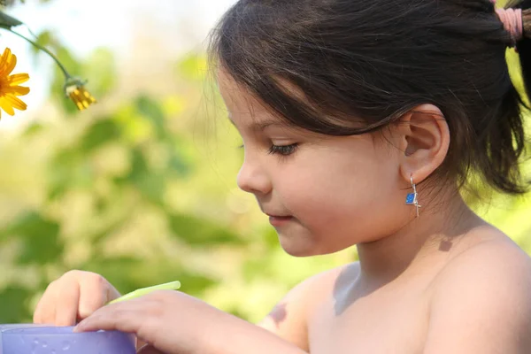 Gülümseyen küçük sevimli kız bulanık doğal bir arka planda yaz masasında oturuyor.