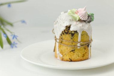 Beyaz şekerli Ortodoks Paskalya pastası ve bir tepside halatla bağlanmış şekerlemeler ve kapta bahar çiçekleri.