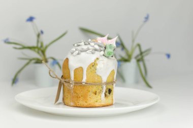 Beyaz şekerli Ortodoks Paskalya pastası ve bir tepside halatla bağlanmış şekerlemeler ve kapta bahar çiçekleri.