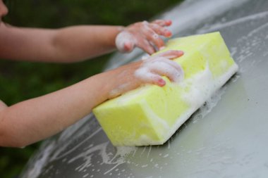 Köpüklü küçük bir çocuğun eli arabanın kaputunu yıkıyor.