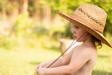Hasır şapkalı şirin bir çocuk boynundaki ipi tutup uzaklığa bakıyor. Üzüm bağında harika çocukluk anları