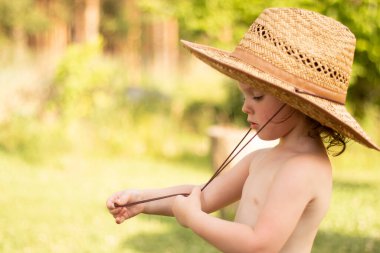 Hasır şapkalı şirin bir çocuk boynunu eğip aşağıya bakıyor. Üzüm bağında harika çocukluk anları