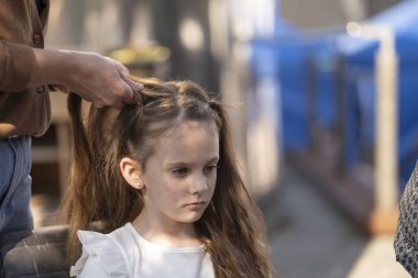 Uzun açık kahverengi saçlı üzgün küçük bir kız için saç stili yapan kadın elleri açık hava masasında oturuyor. Bakım ve annelik kavramı..