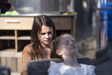 Anne, yaz kafesinde bir masada birlikte otururken kızının saçını yapıyor. Bakım ve aile şefkati kavramı.