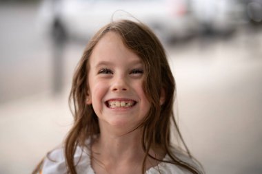 Uzun saçlı, açık havada dişlerini gösteren güzel bir kız. Geçmişi bulanık. Çocukluk ve diş sağlığı kavramı..