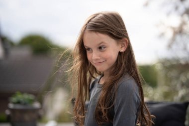 Açık kahverengi saçlı, siyah uzun kollu bir kız. Yazlık terasta komik suratlar yapıyor. Doğal ışık, fotokopi odası. Çocukluk kavramı, oyunculuk ve gerçek duygu..