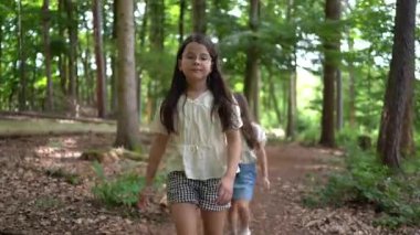 4K gerçek zamanlı bir videoda iki kız yazın bir orman yolunda köpekle yürüyor. Doğada çocukluk, dostluk ve özgürlük kavramı