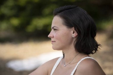 Güzel, koyu renk saçlı, yumuşak dudaklı, mesafeye bakan bir kadın, bulanık arkaplan ve kopyalama alanı olan duygusal bir plaj portresi.