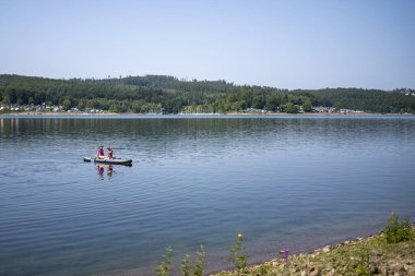 İki mutlu gülümseyen kızın yan görüntüsü can yeleği giymiş SUP sörf tahtasıyla sahile doğru kürek çekerken, fotokopi alanı ile neşeli yaz çocukluk macerası.