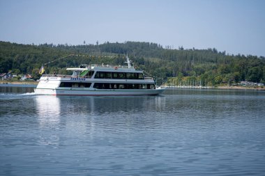 Sorpsee, NRW, Almanya. 13 Ağustos 2025. Turistlerle dolu küçük bir feribot göl kenarına taşınıyor, yaz tatili seyahati ve fotokopi alanı ile huzurlu bir gezinti.